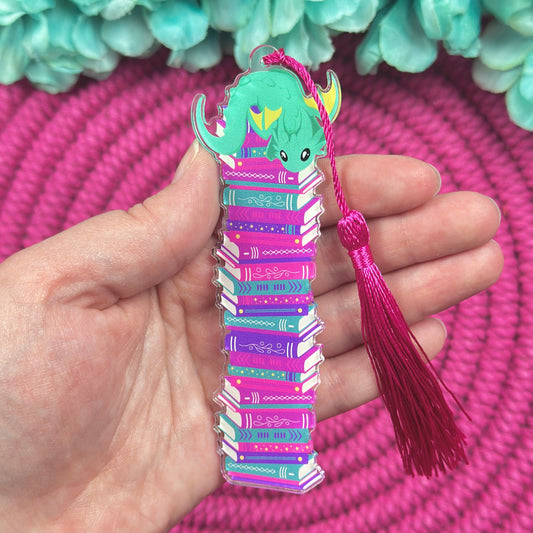 Colorful dragon bookmark with a tassel held by a hand against a pink and blue-green floral background