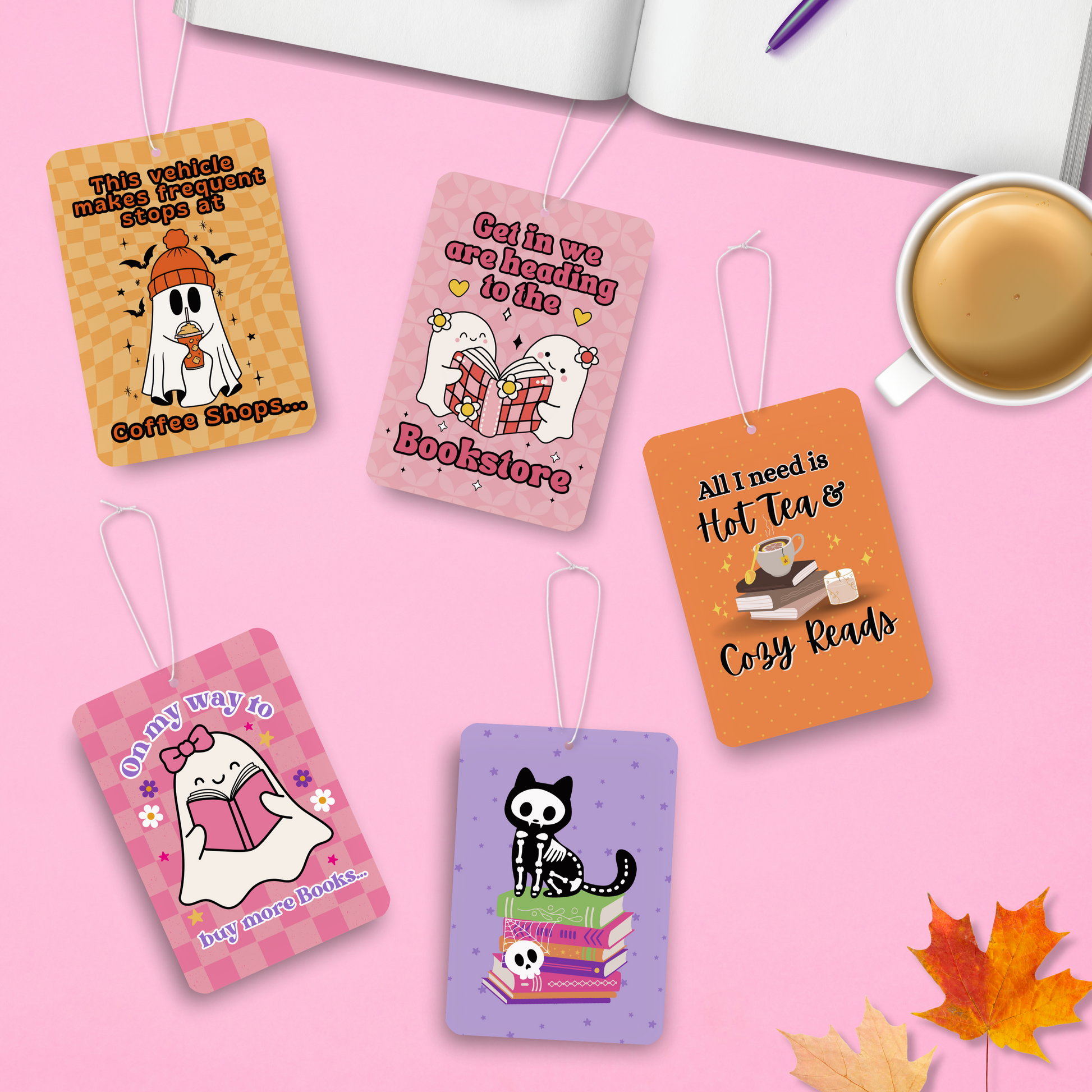 Set of 5 colorful bookish Halloween-themed car air fresheners laying flat on a pink background with an open book, coffee cup and autumn leaves.