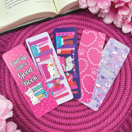 Set of colorful bookmarks with cat and dog designs on a pink textured surface with pink flowers and an open book.