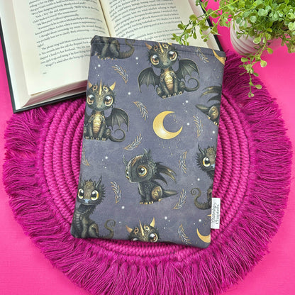 Book with dragon pattern on a pink woven mat, open book and plant in the background