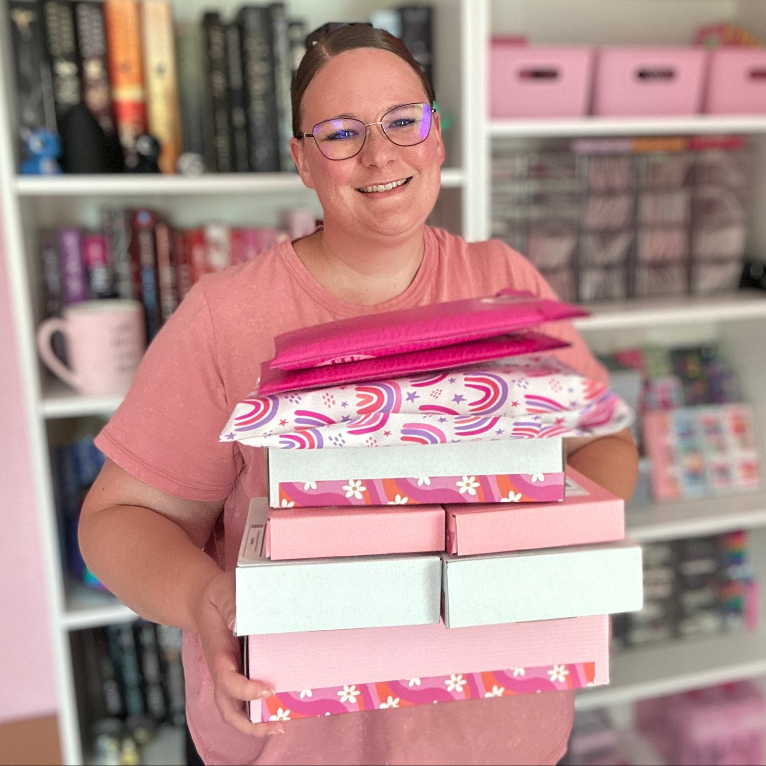 Person holding a stack of pink and white boxes in a room with shelves and books.