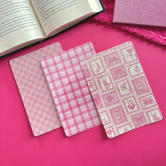 Three pink patterned Kindle case inserts on a pink surface with an open book.