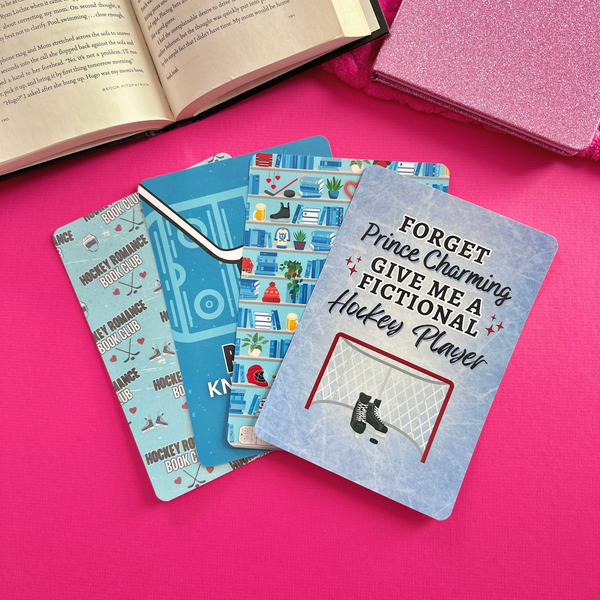 Four eReader inserts with hockey-themed designs laying on a pink surface next to an open book.