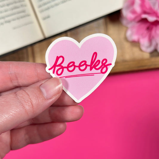 Heart-shaped sticker with 'Books' text held by a hand against a pink background