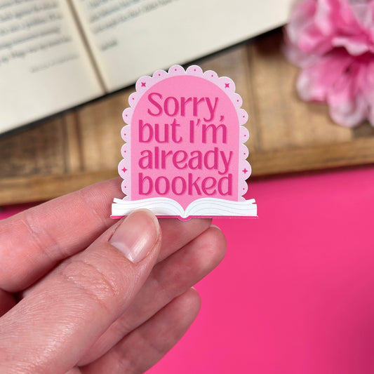 Pink sticker with 'Sorry, but I'm already booked' text held by a hand against a pink background.