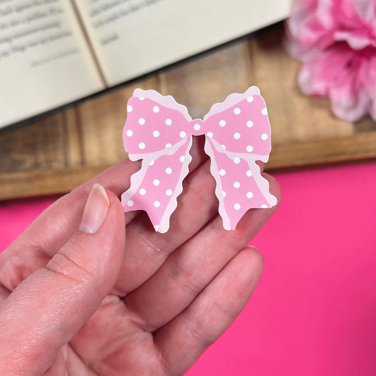Pink polka dot bow-shaped vinyl sticker  held in a hand with a pink background