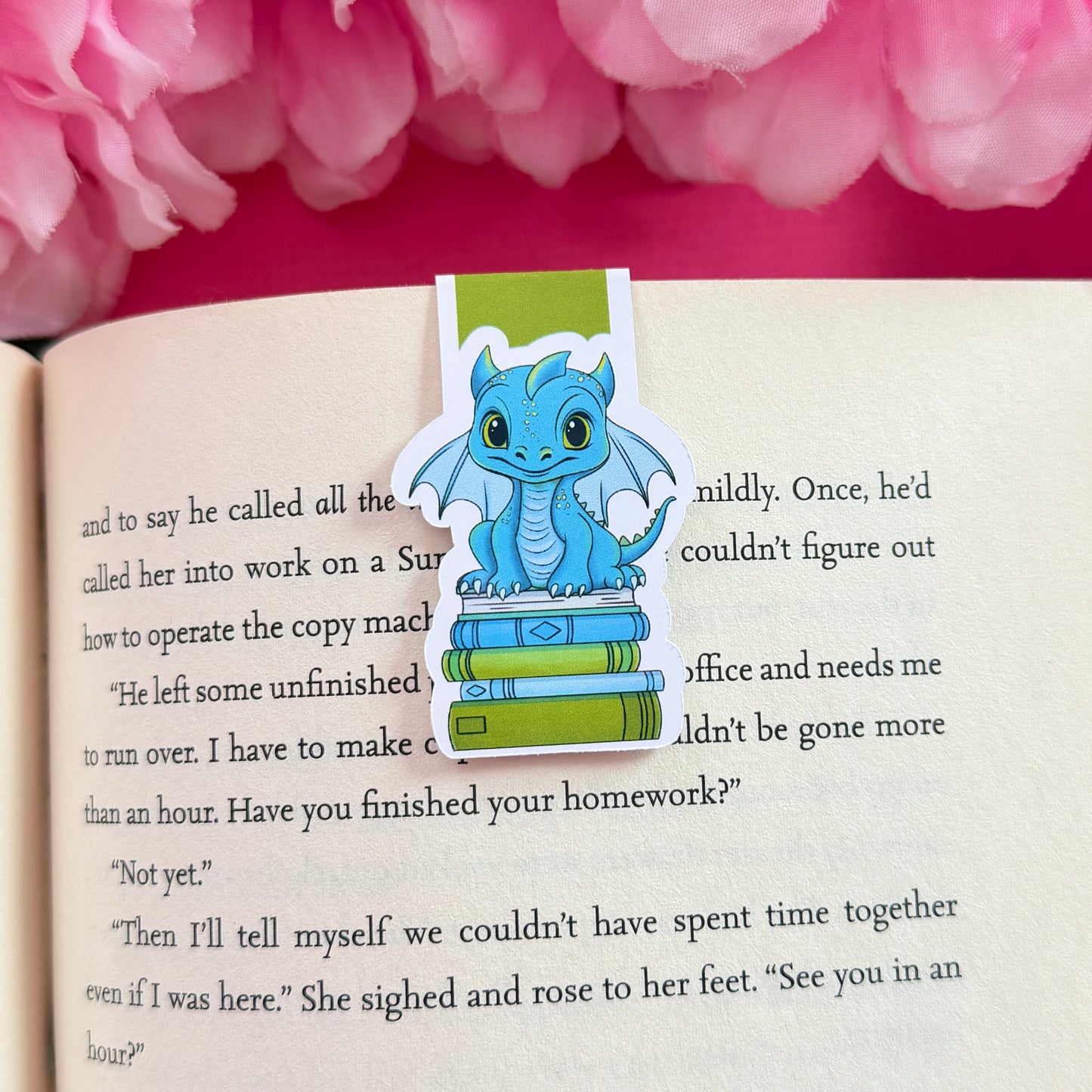 Magnetic bookmark with a blue and green dragon design on an open book surrounded by pink flowers
