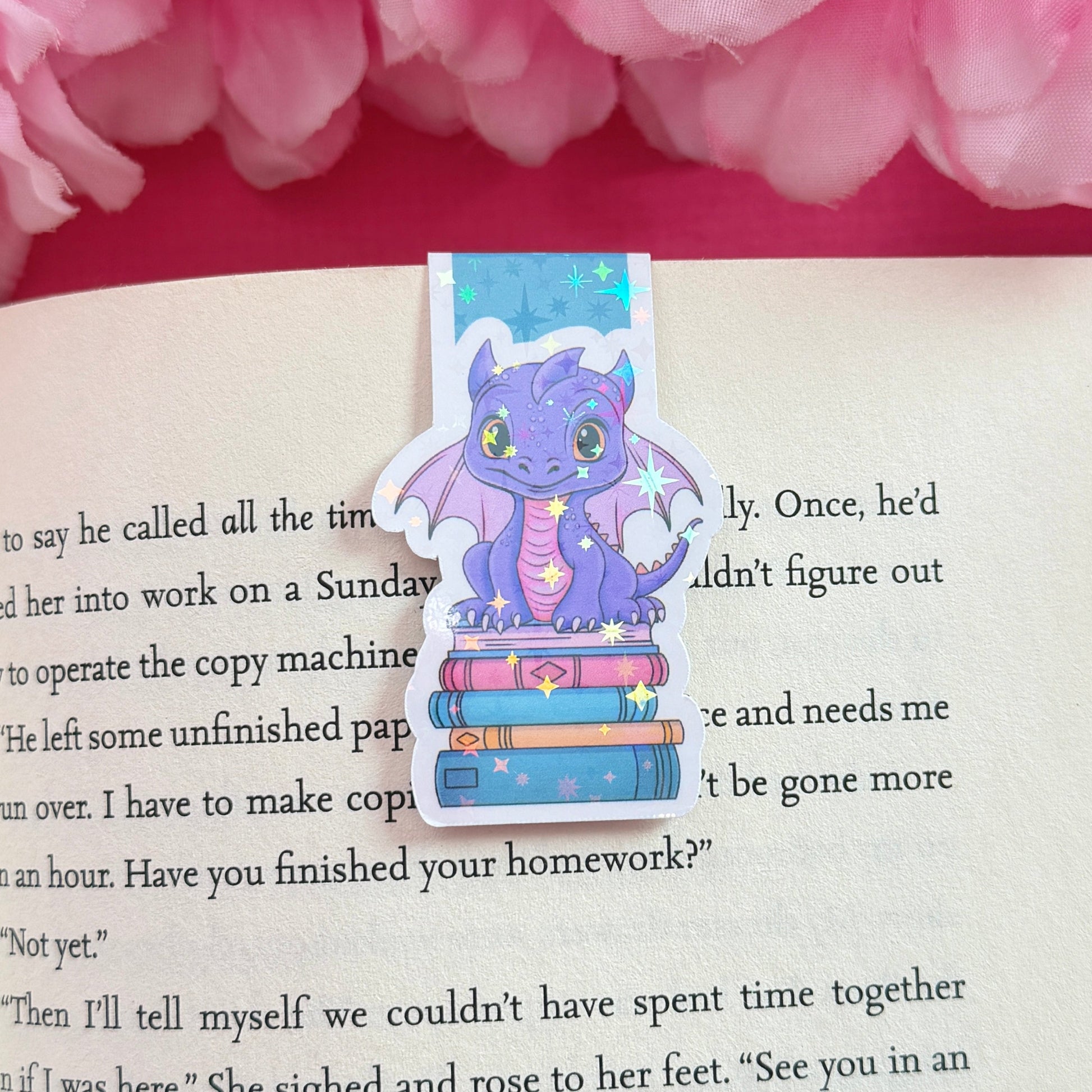 Magnetic bookmark with a purple and pink dragon design on an open book surrounded by pink flowers. The bookmark has a holographic star finish.