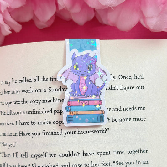 Magnetic bookmark with a purple and pink dragon design on an open book surrounded by pink flowers. The bookmark has a holographic star finish.