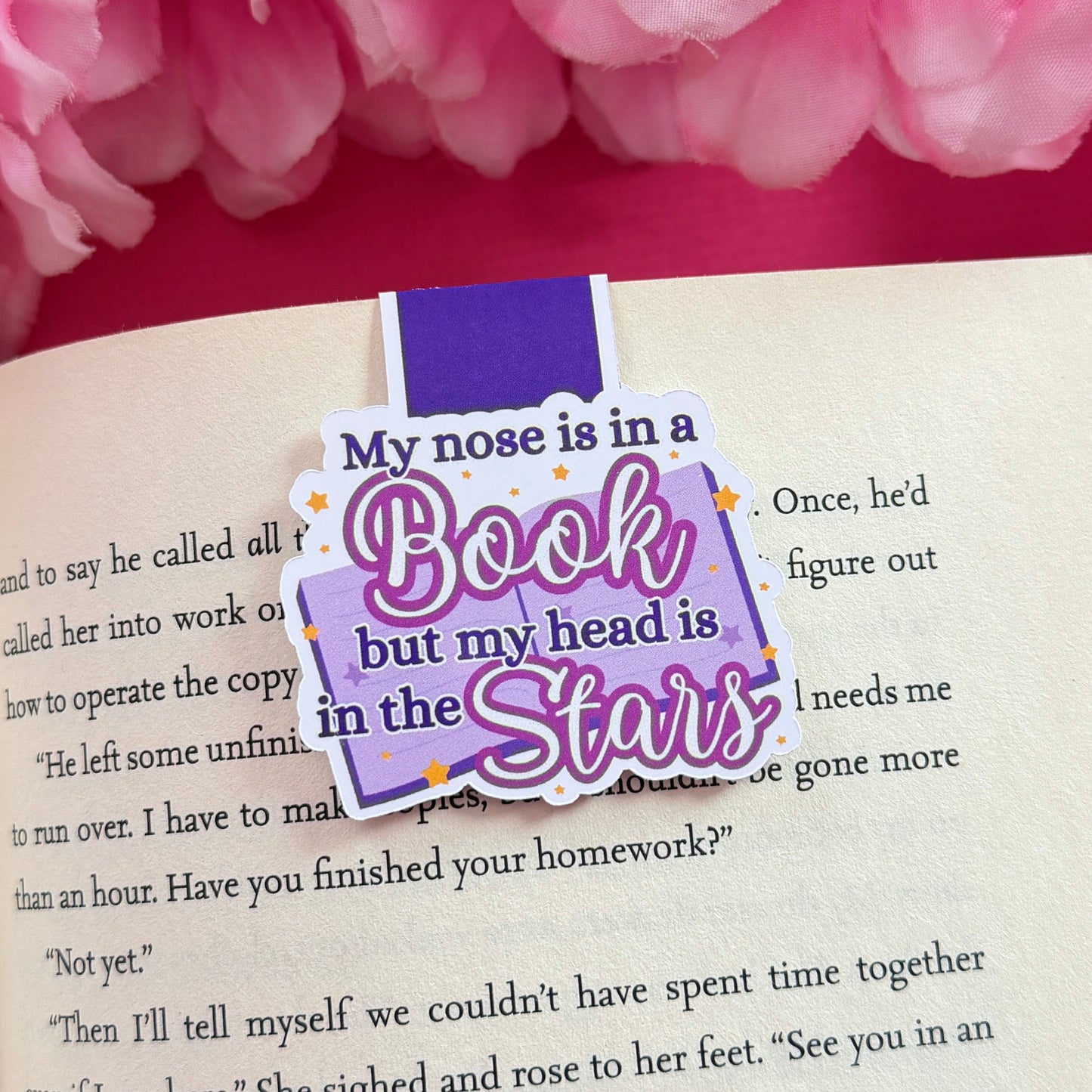 Magnetic bookmark that has a late night reader design. The bookmark is on an open book surrounded by pink flowers.