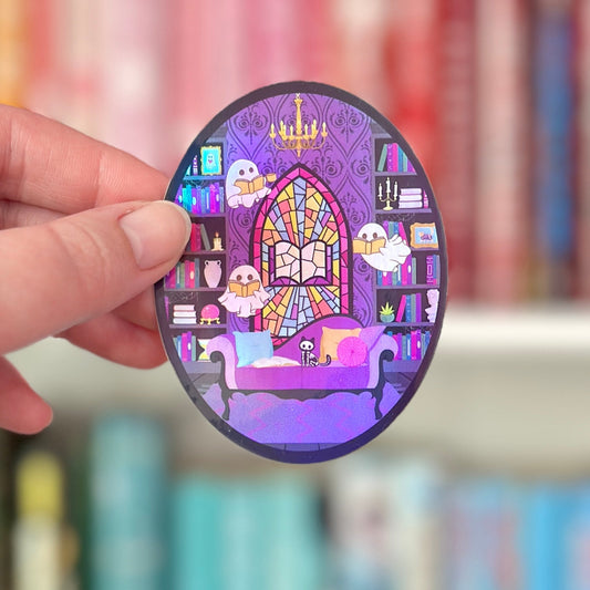 Oval-shaped sticker with a haunted library-themed design held by a hand against a blurred bookshelf background.