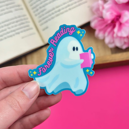 Cartoon ghost sticker with 'Forever Reading' text held by a hand on a pink surface.